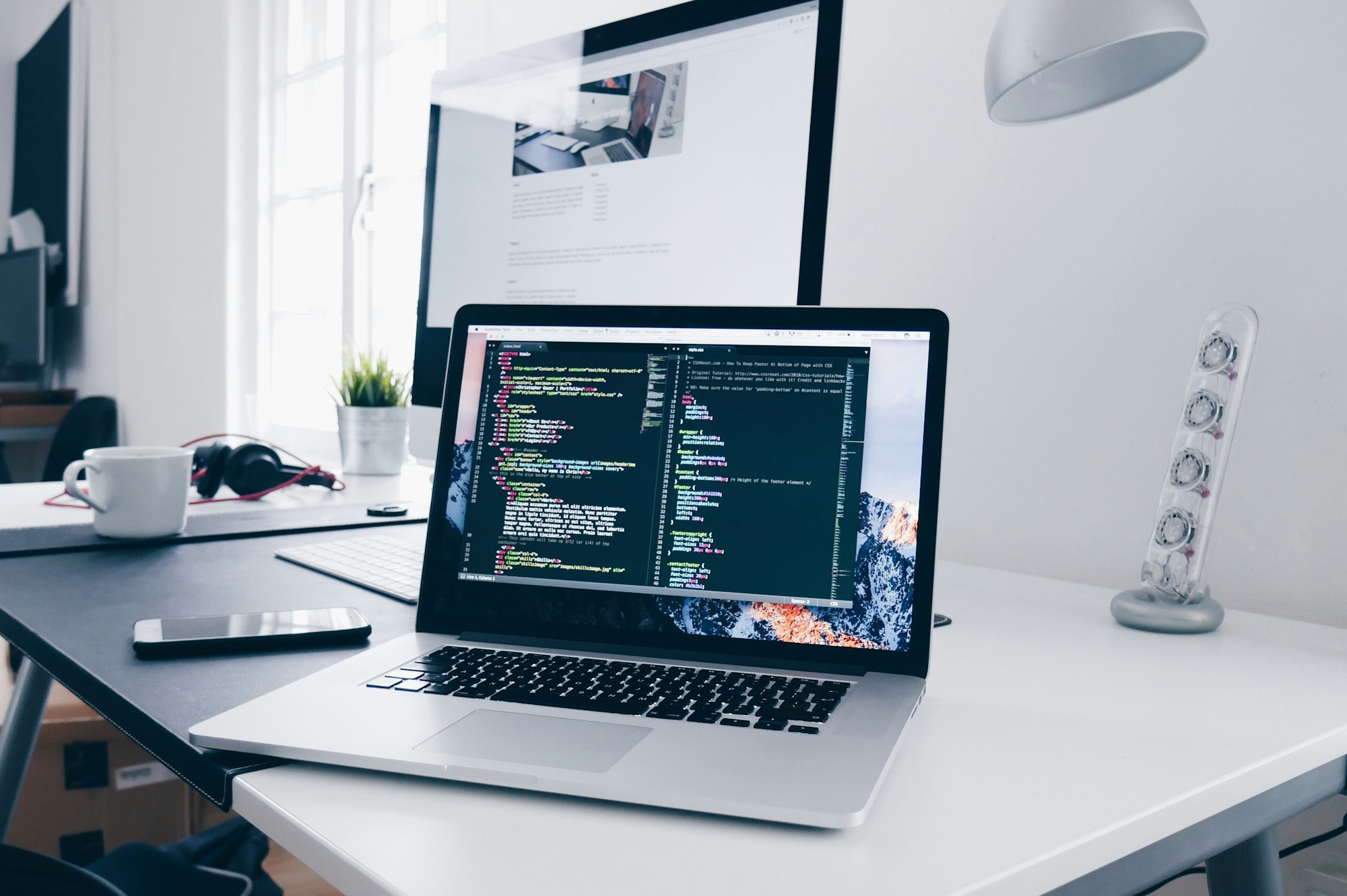 A laptop and monitor on a desk showing a code editor during a website build